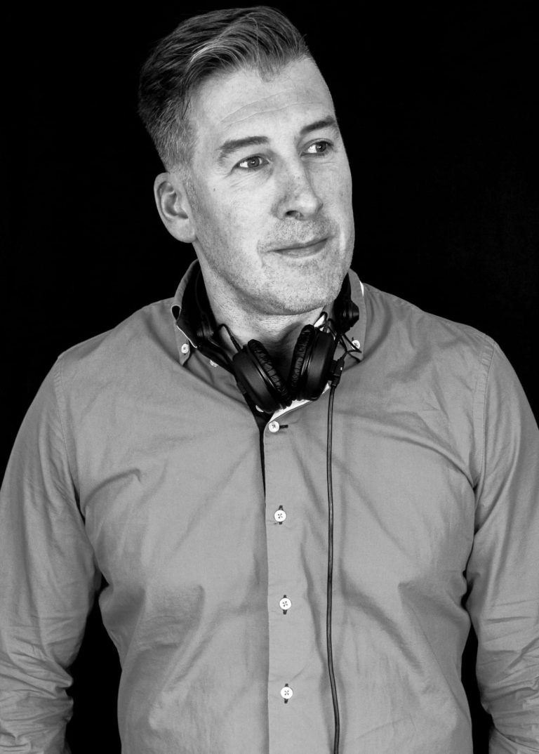 DJ Ronny LE. 1 Mann mit Kopfhörern und Hemd, schaut zufrieden und nachdenklich nach rechts.