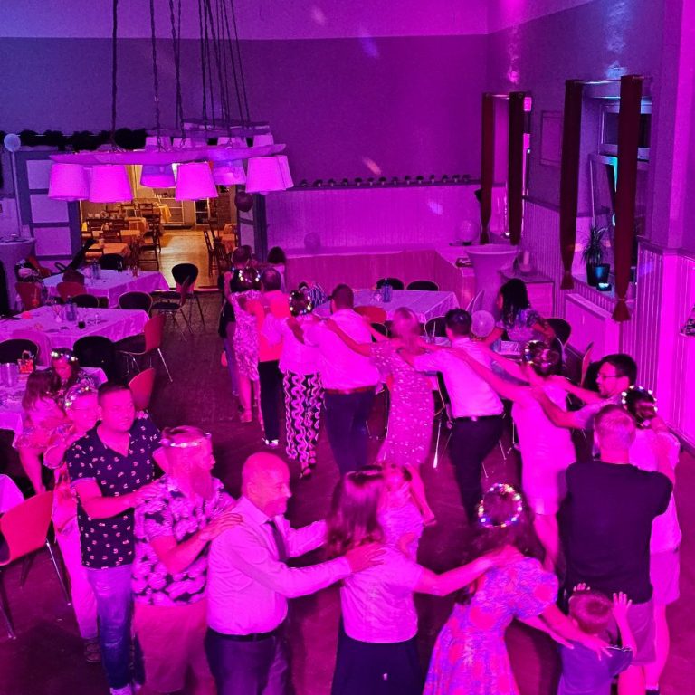 Feiernde Menschen in bunten Outfits, umgeben von festlicher Beleuchtung.