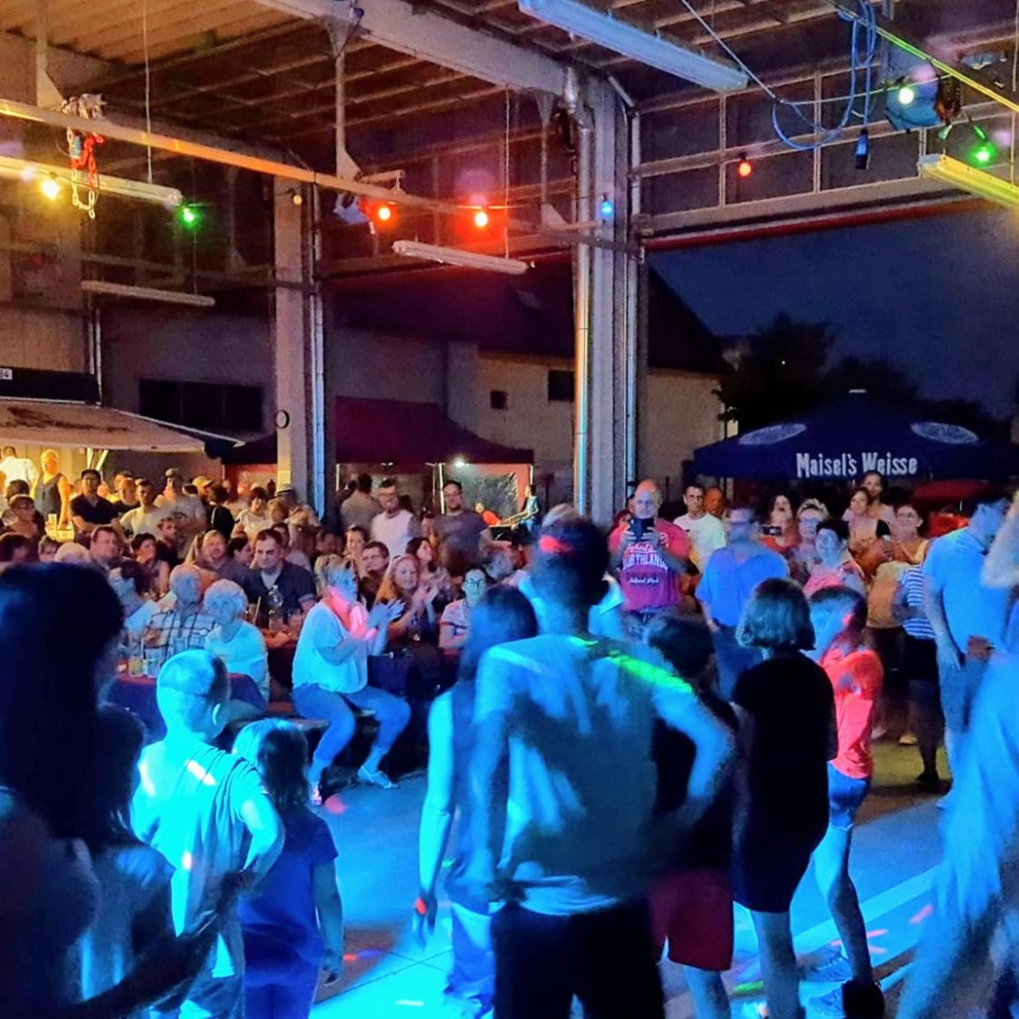 Firmenfeier Feuerwehrball Wiederitzsch Bunte Party mit Menschen tanzend und feiernd in einem Feuerwehgerätehaus bei Nacht.