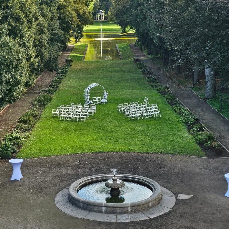 Eleganter Garten mit einer Rasenfläche, Stühlen für eine Zeremonie und einem Brunnen.