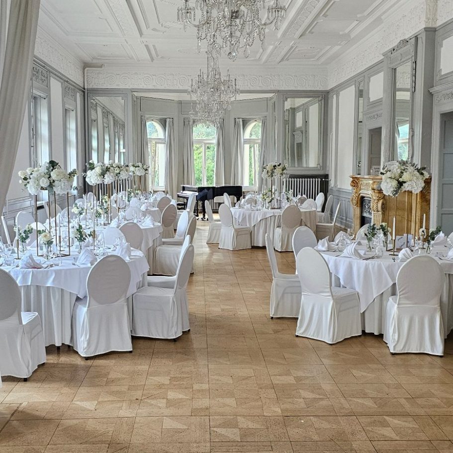 Eleganter Saal mit weißen Tischen, Blumenarrangements und einem Klavier.