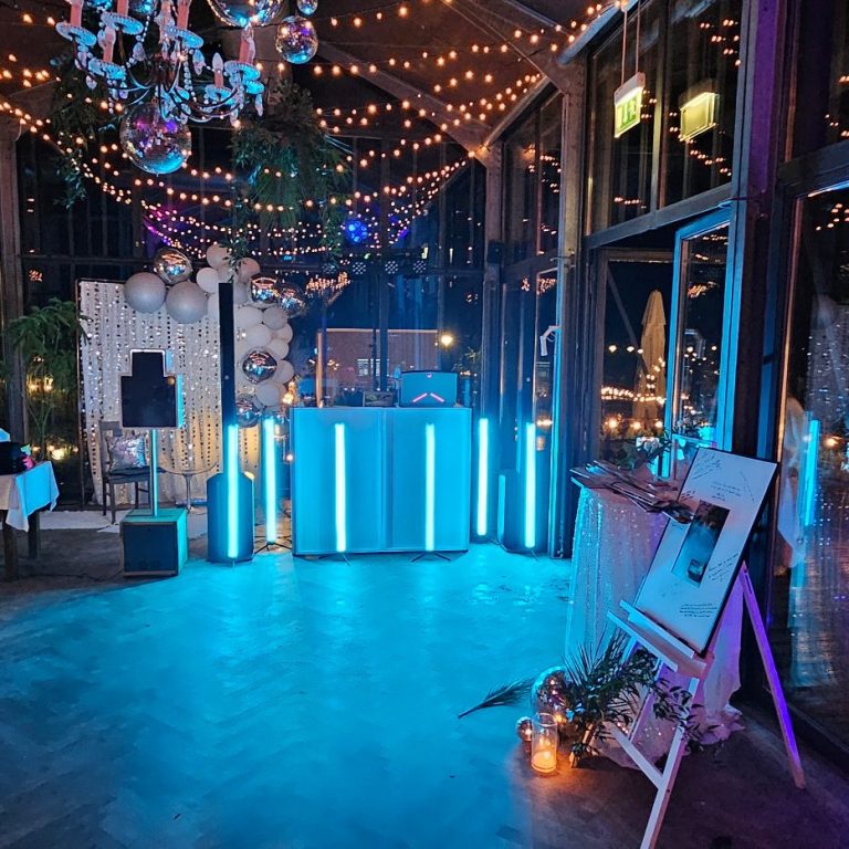 Stilvolles Ambiente mit blauen Lightsticks, Dj Pult und festlicher Dekoration.