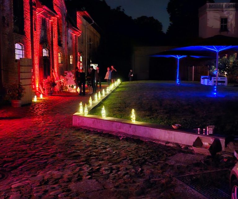 Beleuchtetes Ambiente einer Veranstaltung mit Wasserfontänen und Menschen, nachts.