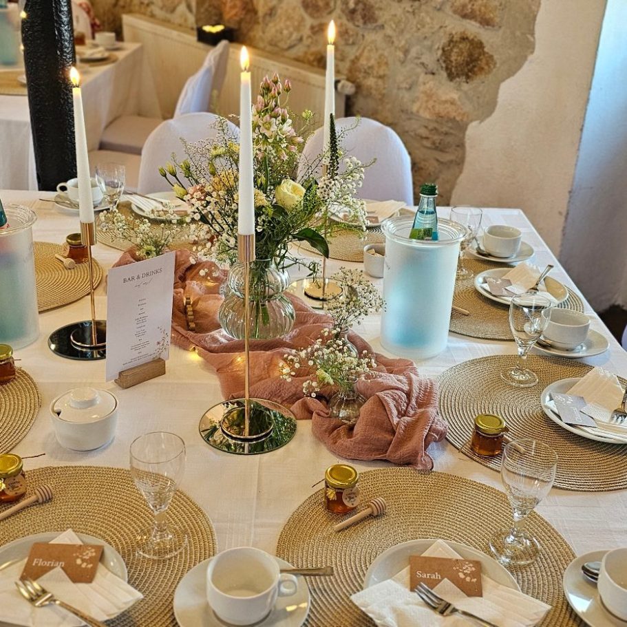 Tischdeko für ein festliches Essen mit Blumen, Kerzen und gedecktem Geschirr.